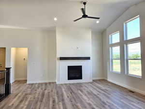 Unfurnished living room featuring a fireplace, light wood-type flooring, ceiling fan, and a wealth of natural light