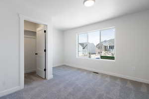 Unfurnished bedroom featuring carpet flooring, a walk in closet, and a closet