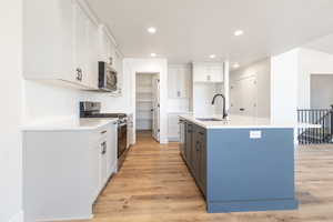 Kitchen featuring light wood-type flooring, sink, an island with sink, white cabinetry, and stainless steel appliances