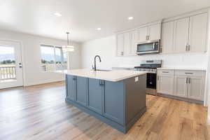 Kitchen with an island with sink, sink, decorative light fixtures, light hardwood / wood-style flooring, and appliances with stainless steel finishes