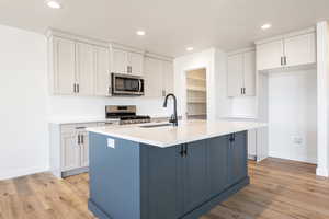 Kitchen featuring an island with sink, sink, white cabinetry, stainless steel appliances, and light hardwood / wood-style floors