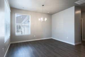 Unfurnished room with dark wood-type flooring and a chandelier