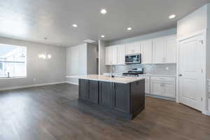 Kitchen featuring appliances with stainless steel finishes, decorative backsplash, dark hardwood / wood-style floors, white cabinetry, and a center island with sink