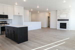 Kitchen featuring appliances with stainless steel finishes, light wood-type flooring, a center island, white cabinetry, and a stone fireplace