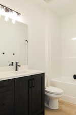 Full bathroom with vanity, toilet, wood-type flooring, and washtub / shower combination