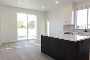 Kitchen featuring light wood-type flooring, tasteful backsplash, sink, white cabinets, and a center island