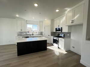 Kitchen with wood-type flooring, sink, white cabinets, a kitchen island, and appliances with stainless steel finishes