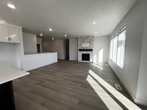 Unfurnished living room with a stone fireplace and dark wood-type flooring