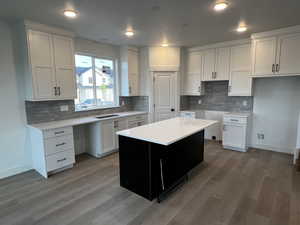 Kitchen with light hardwood / wood-style floors, backsplash, sink, a center island, and white cabinets