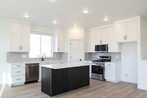 Kitchen with a center island, sink, light hardwood / wood-style floors, white cabinetry, and stainless steel appliances