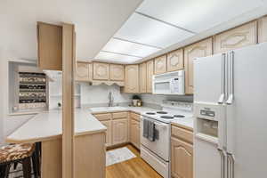 Kitchen featuring light brown cabinets, white appliances, kitchen peninsula, light hardwood / wood-style floors, and sink