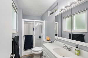 Bathroom featuring vanity, an enclosed shower, a textured ceiling, and toilet