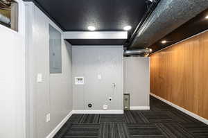 Clothes washing area featuring dark colored carpet, hookup for a washing machine, electric panel, and wooden walls