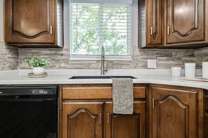 Kitchen featuring sink, dishwasher, tasteful backsplash, and light stone counters