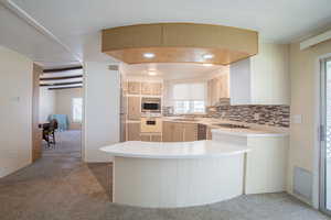 Kitchen featuring kitchen peninsula, backsplash, stainless steel appliances, light carpet, and sink