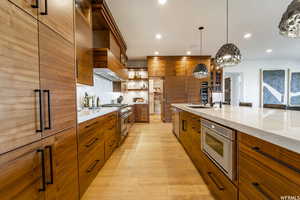 Kitchen with decorative light fixtures, range with two ovens, sink, light hardwood / wood-style flooring, and backsplash