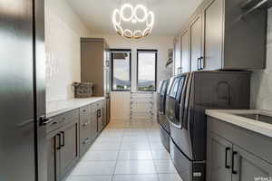 Laundry area with cabinets, a chandelier, washer and dryer, and light tile patterned floors