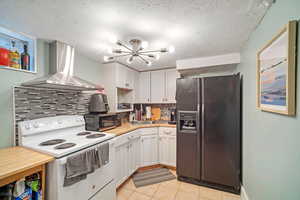 Kitchen with wall chimney range hood, white cabinetry, black appliances, and backsplash