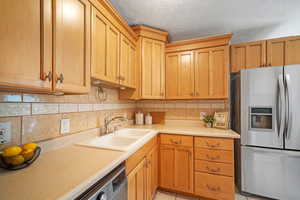 Kitchen with light tile patterned floors, a textured ceiling, backsplash, stainless steel fridge, and sink