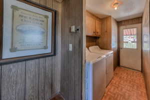 Clothes washing area featuring washer and clothes dryer, wood walls, cabinets, and light parquet flooring