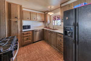 Kitchen featuring black appliances, pendant lighting, sink, and light parquet flooring