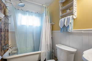 Bathroom with shower / tub combo with curtain, wooden walls, and toilet