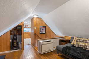 Sitting room with vaulted ceiling, a textured ceiling, wooden walls, and hardwood / wood-style floors