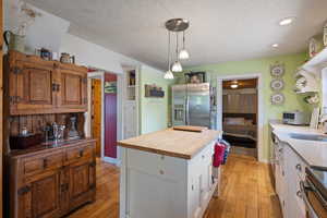 Kitchen with wood counters, light wood-type flooring, stainless steel fridge with ice dispenser, a center island, and white cabinetry