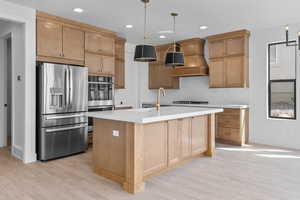 Kitchen featuring an island with sink, hanging light fixtures, stainless steel appliances, and light hardwood / wood-style flooring