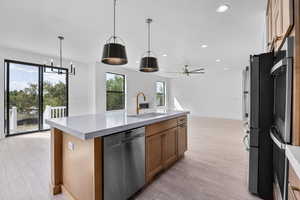 Kitchen with hanging light fixtures, light wood-type flooring, stainless steel appliances, ceiling fan, and a kitchen island with sink