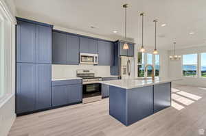 Kitchen featuring a kitchen island with sink, decorative light fixtures, light hardwood / wood-style flooring, and appliances with stainless steel finishes