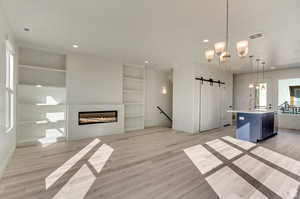 Unfurnished living room featuring built in features, light wood-type flooring, an inviting chandelier, and a barn door