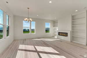 Unfurnished living room featuring a healthy amount of sunlight, built in shelves, and light wood-type flooring