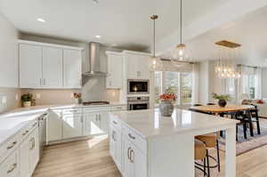 Kitchen featuring white cabinetry, light hardwood / wood-style flooring, tasteful backsplash, wall chimney range hood, and stainless steel appliances