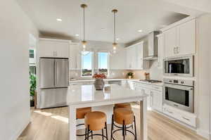 Kitchen featuring stainless steel appliances, white cabinets, decorative backsplash, wall chimney exhaust hood, and light hardwood / wood-style floors