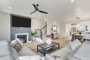 Living room featuring a fireplace, light wood-type flooring, and ceiling fan with notable chandelier