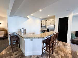 Kitchen featuring carpet flooring, a breakfast bar, appliances with stainless steel finishes, and kitchen peninsula