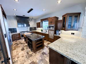 Kitchen featuring light stone countertops, sink, appliances with stainless steel finishes, decorative light fixtures, and a center island with sink