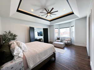 Bedroom with ceiling fan, dark hardwood / wood-style floors, and a tray ceiling