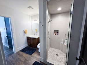 Bathroom with tiled shower, vanity, toilet, and hardwood / wood-style floors