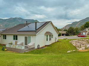 Rear view of property with solar panels, a mountain view, and a lawn