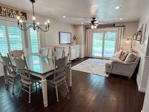 Dining space with a textured ceiling, ceiling fan with notable chandelier, and dark wood-type flooring