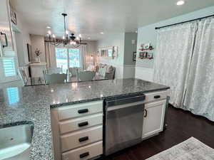 Kitchen featuring dark stone countertops, an inviting chandelier, white cabinets, stainless steel dishwasher, and dark hardwood / wood-style floors