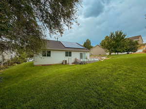 Rear view of property featuring a lawn, central AC unit, and solar panels