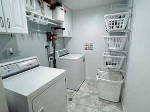 Laundry area featuring light tile patterned floors, washer and clothes dryer, and cabinets