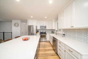 Kitchen with appliances with stainless steel finishes, white cabinets, sink, backsplash, and light laminate floors