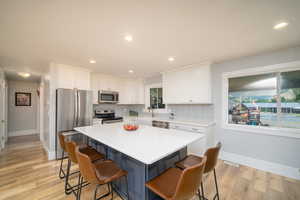 Kitchen with light laminate flooring, tasteful backsplash, white cabinets, a center island, and appliances with stainless steel finishes