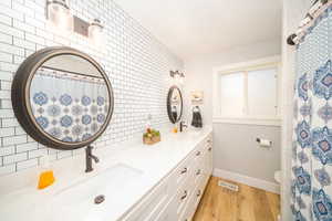 Bathroom featuring tasteful backsplash, double vanity, toilet, tile walls, and laminate flooring