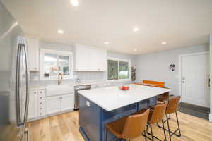 Kitchen with appliances with stainless steel finishes, light laminate flooring, white cabinets, sink, and backsplash