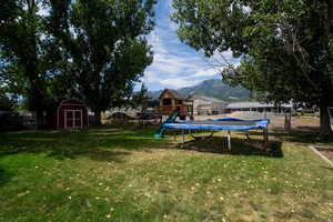 View of yard featuring a mountain view, a trampoline, a playground, and a shed